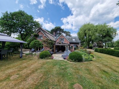 a charming home featuring a thatched roof and wooden canopy set amongst a green garden scaled