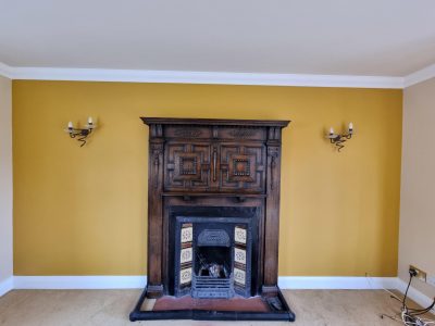 a vibrant yellow wall with a wooden mantlepiece and rustic fireplace in the centre of the wall